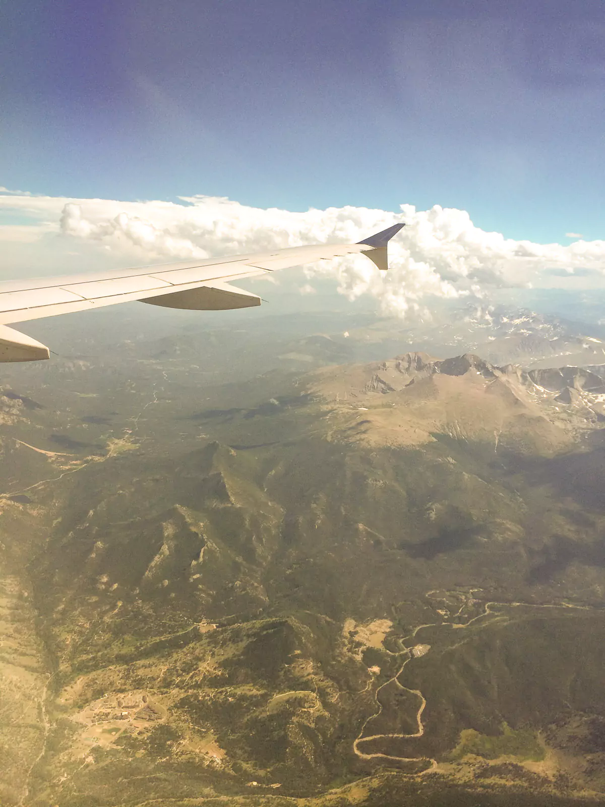 Aerial photo showing rugged mountain peaks and deep valleys covered in greenery, taken from an airplane window over Wyoming. The expansive landscape highlights the state’s dramatic natural terrain.