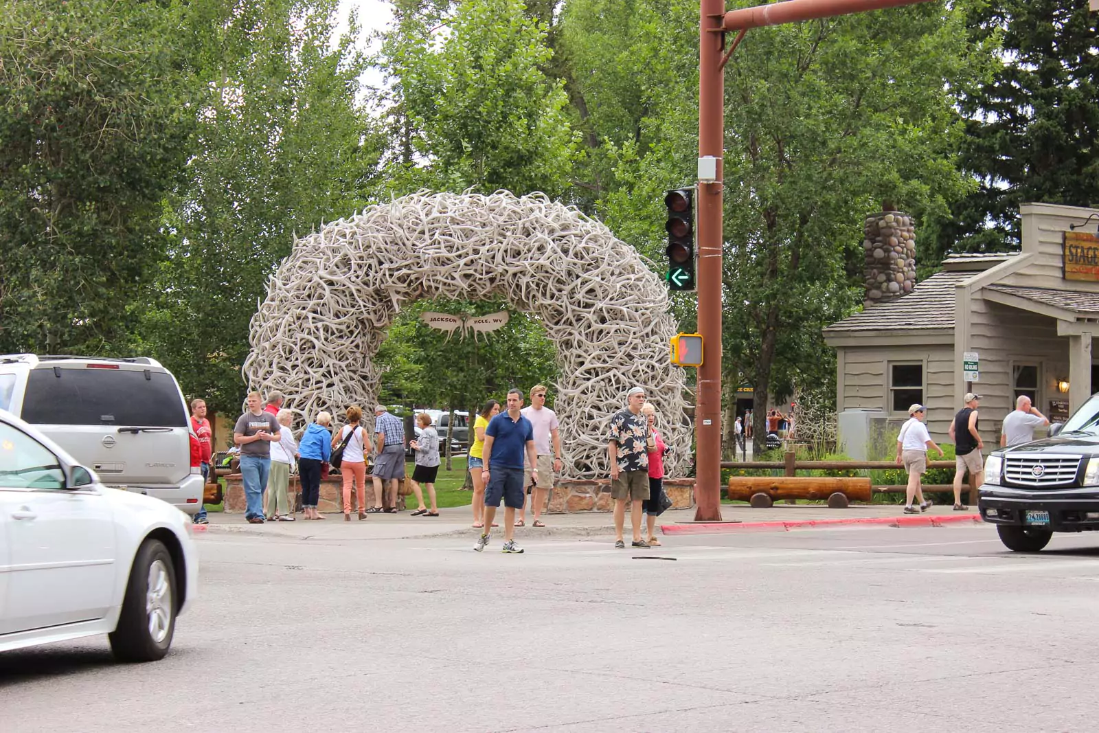A crowd of people walking and gathering near the iconic Antler Arch in Jackson Hole, Wyoming, made of intertwined elk antlers. The lively scene captures the popular western landmark with visitors enjoying the outdoor setting.