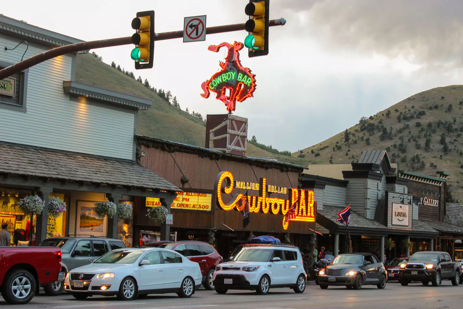 The iconic Million Dollar Cowboy Bar exterior in Jackson Hole, featuring rustic log cabin architecture with a large wooden porch and western-style signage. The historic bar is a popular spot known for its cowboy culture and lively atmosphere.