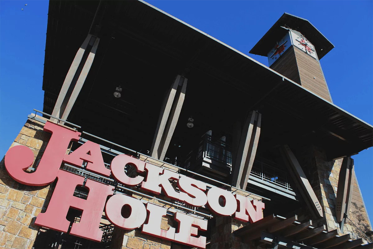 A large sign reading ‘Jackson Hole Mountain Resort’ set against a backdrop of pine trees and blue sky in Wyoming. The sign welcomes visitors to the popular mountain resort destination.