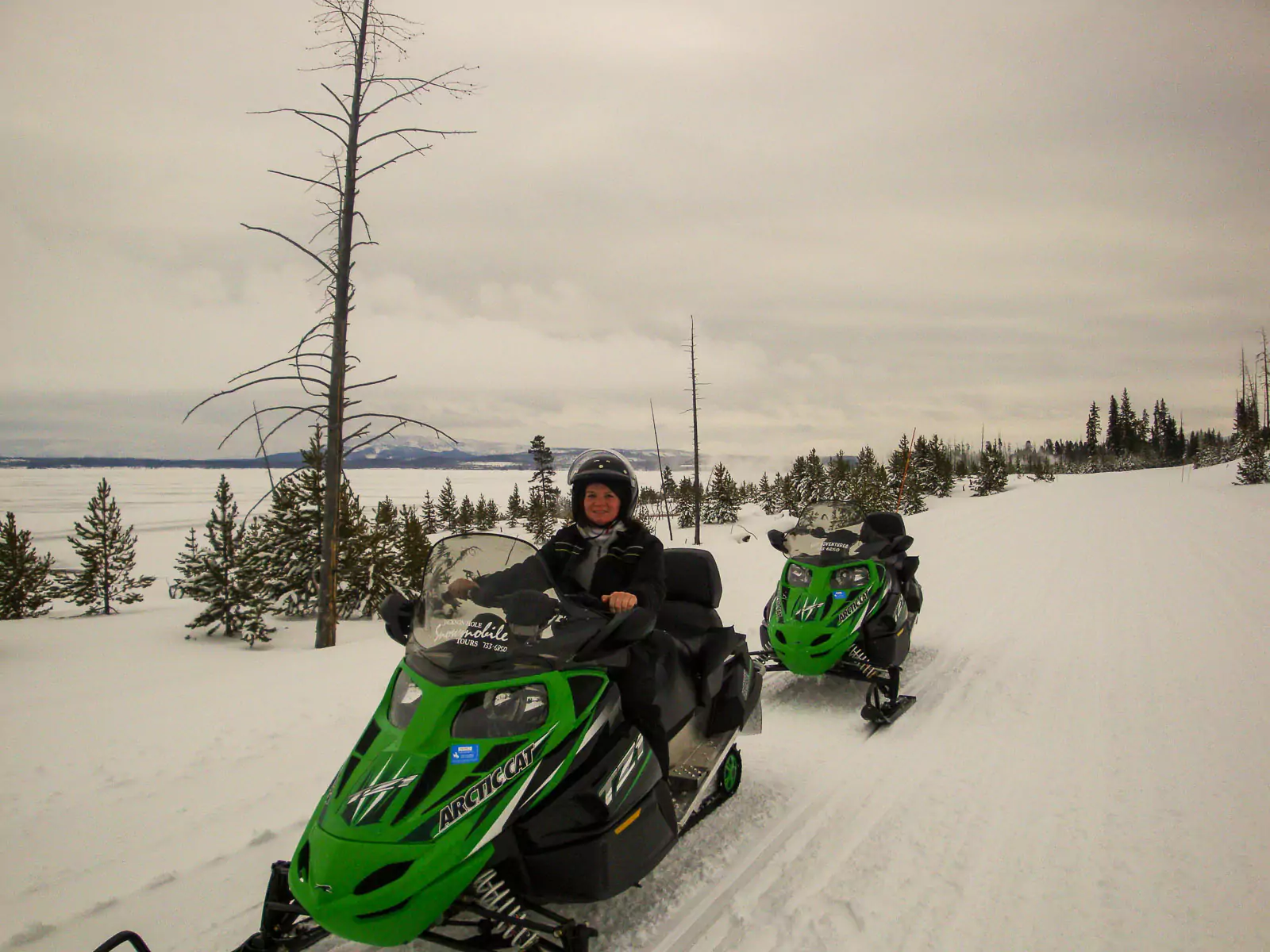 Katie rides a snowmobile through a snowy Yellowstone National Park landscape, bundled up in winter gear against the cold. The scene captures the excitement of exploring the park’s winter wilderness.