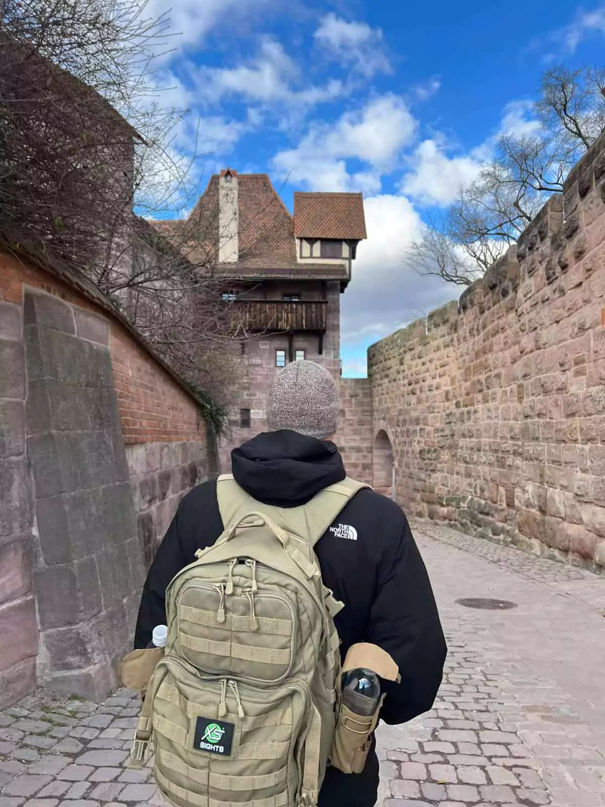 Zack seen from behind walking through the grounds of Nuremberg’s Imperial Castle, surrounded by medieval stone walls, timber-framed buildings, and cobblestone pathways.